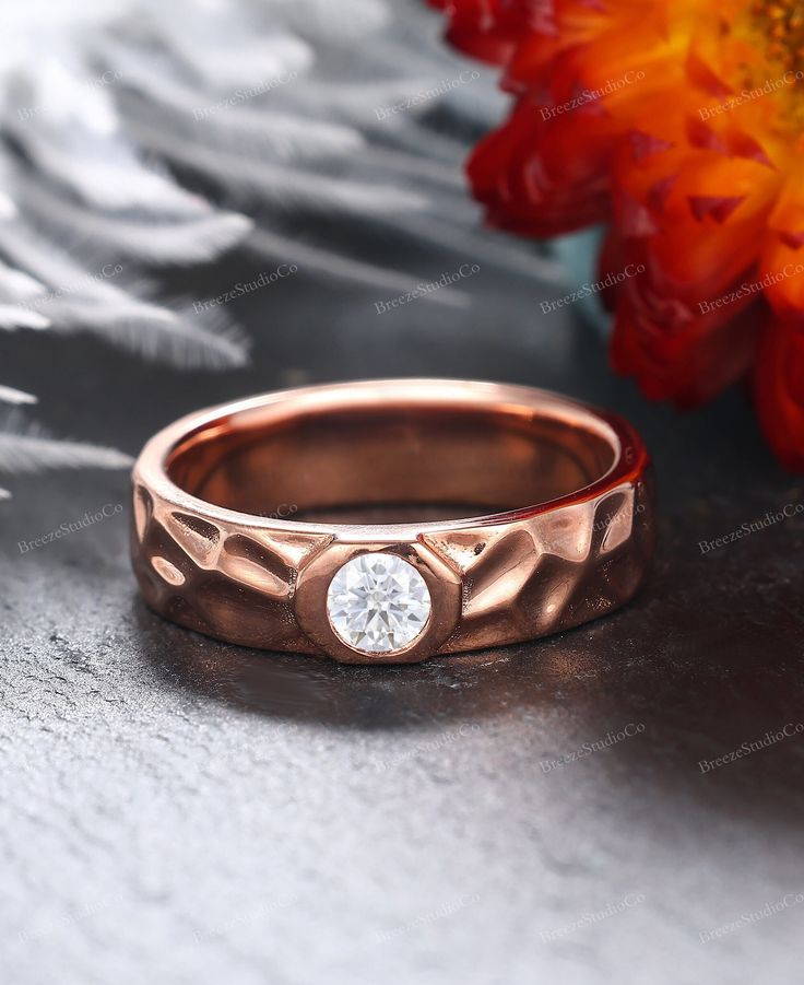 a rose gold wedding ring with a diamond in the center and a flower behind it