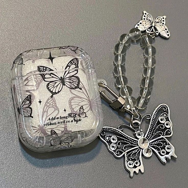 two butterfly shaped key chains are next to a small case with a charm on it