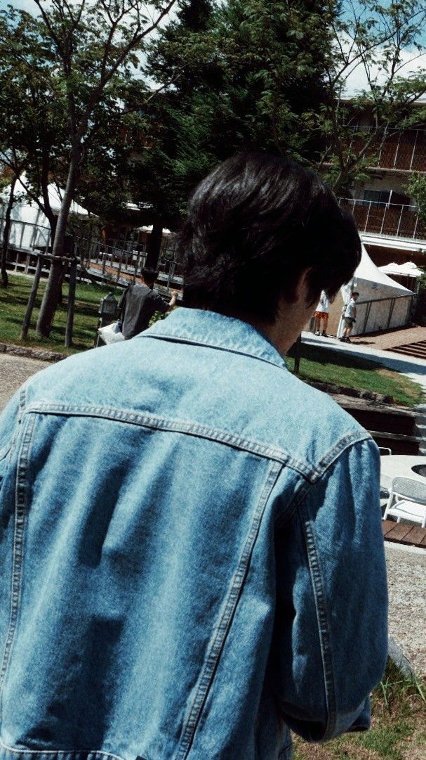 a man wearing a jean jacket is looking down at the ground