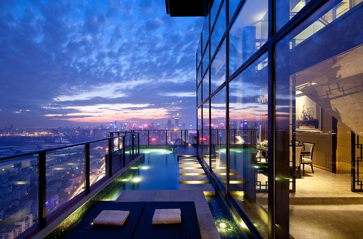 an outdoor swimming pool in front of a large window at night with the city lights lit up