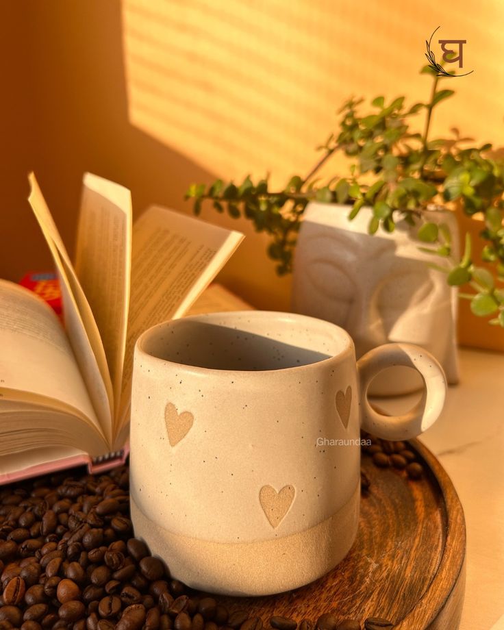 a coffee cup with hearts on it sitting next to an open book and some coffee beans