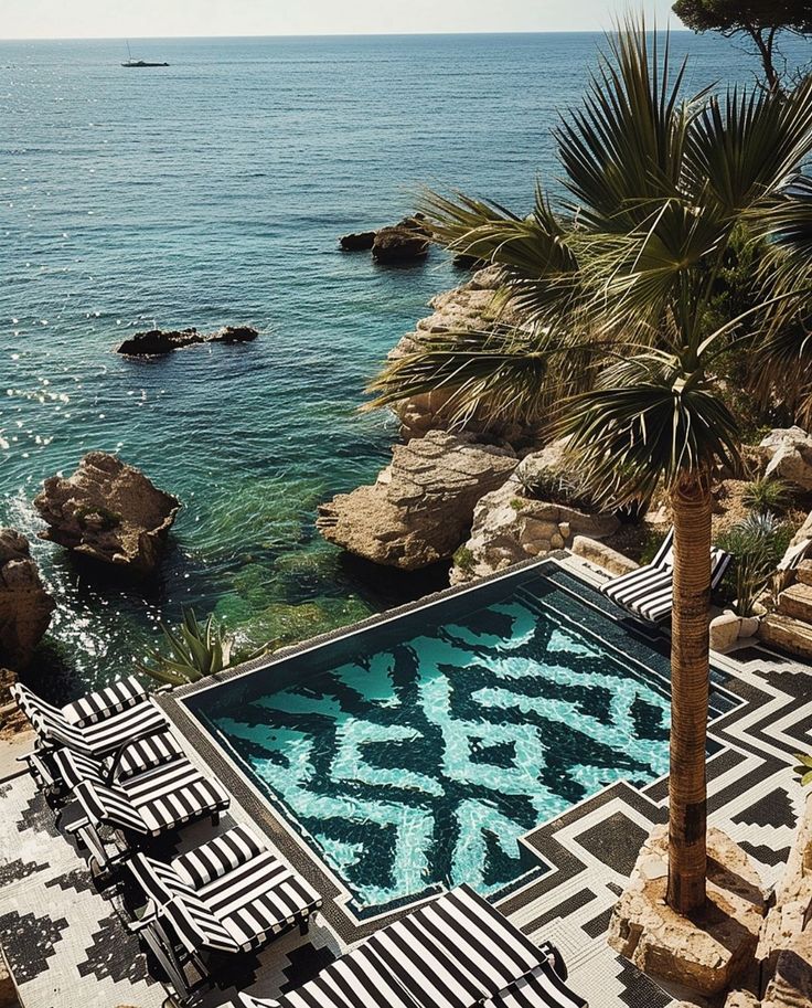 an outdoor swimming pool next to the ocean with lounge chairs and palm trees around it