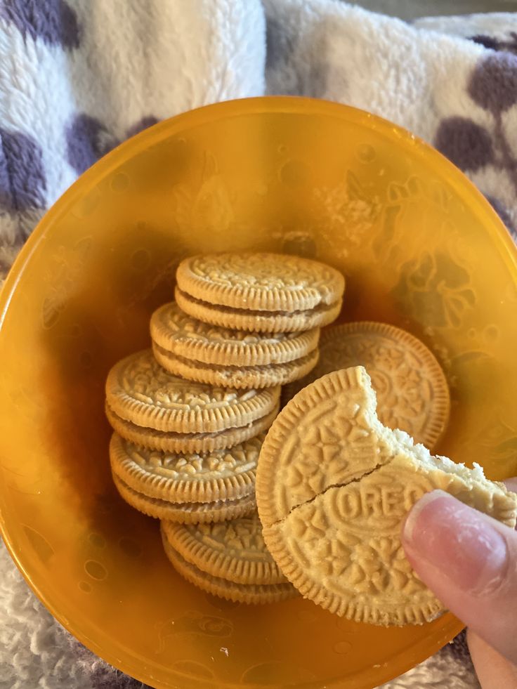 a yellow bowl filled with cookies on top of a blanket next to a person's hand