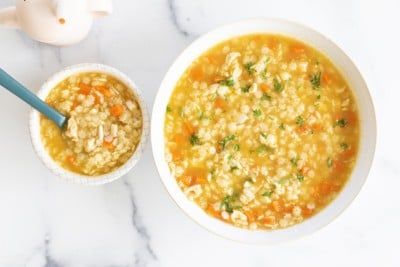 a bowl of soup next to a teapot on a marble counter top with a blue spoon