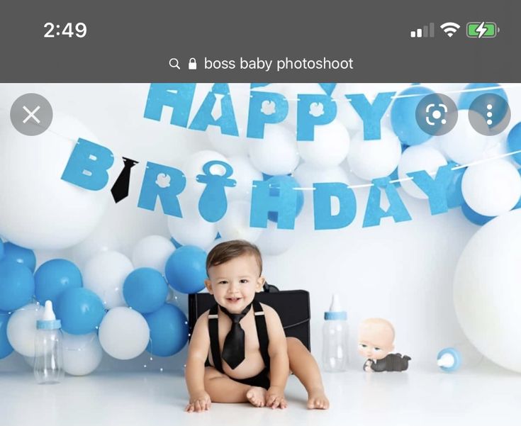 a baby is sitting on the floor in front of blue and white balloons, while wearing a black tie