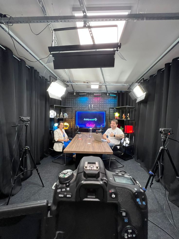 two men sitting at a table in front of camera equipment