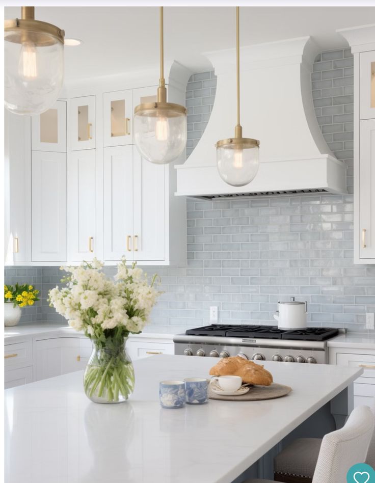 a white kitchen with marble counter tops and gold pendant lights hanging over the stove top