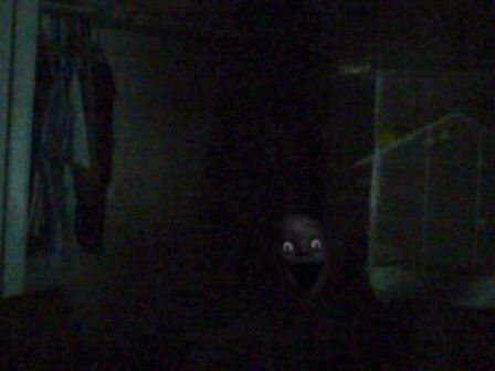 a creepy looking face in the dark by a wall with clothes hanging on it's walls