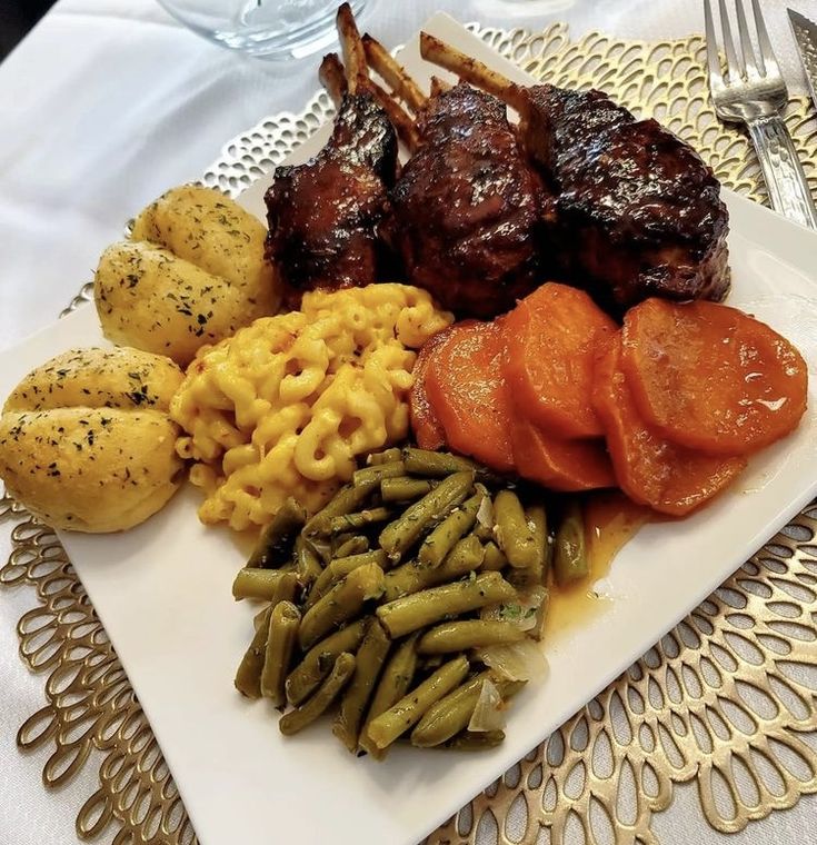 a white plate topped with meat and veggies next to potatoes on a table