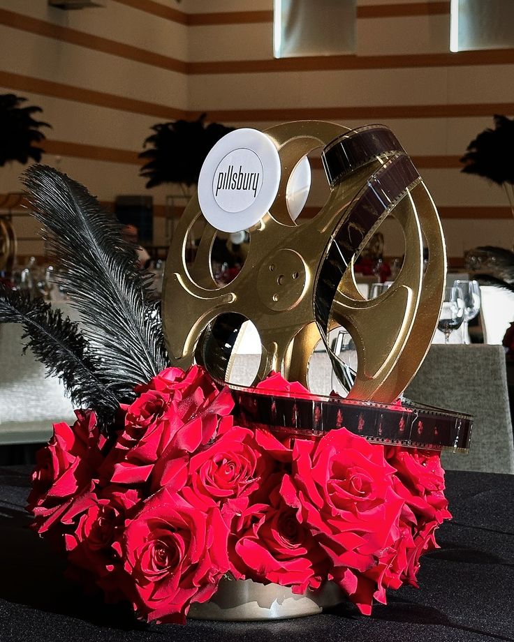 a table with red roses and an old movie reel on it's centerpiece