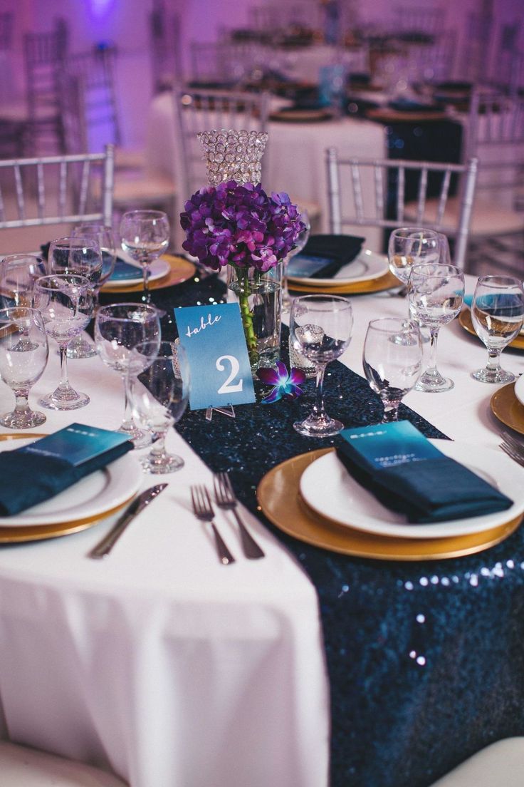 the table is set with blue and gold place settings, silverware, and purple flowers