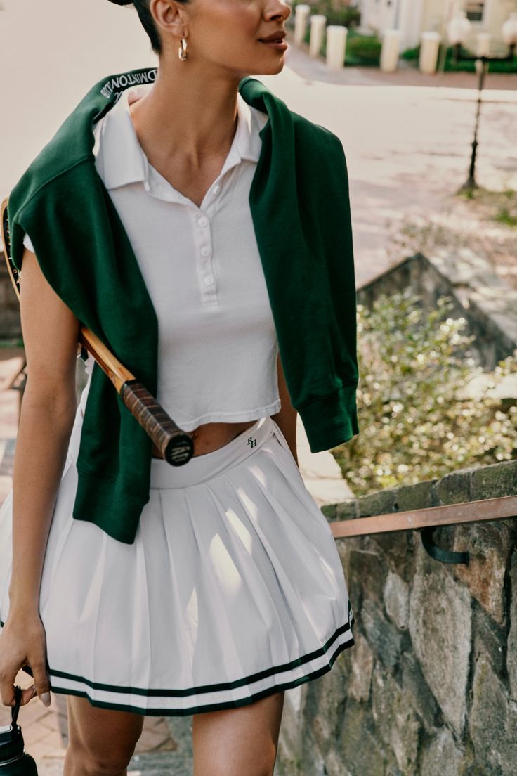 a woman with a tennis racket is walking down the street wearing a skirt and jacket