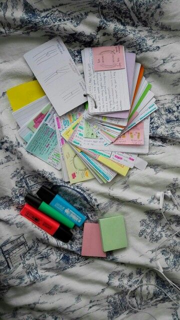 many different colored papers and pens on a bed