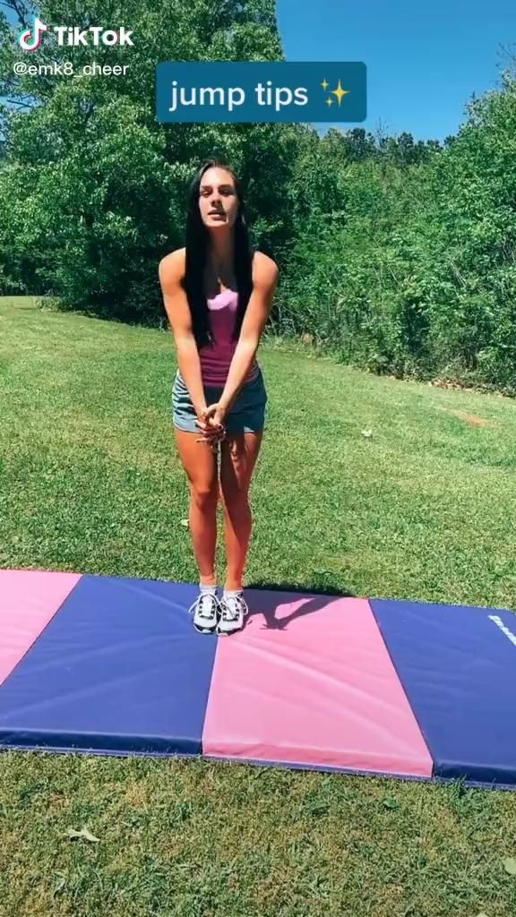 a woman standing on top of a pink and blue mat in the grass with trees behind her