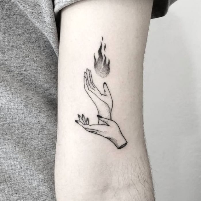 a hand holding a flame tattoo on the left forearm and arm, with two hands reaching for it