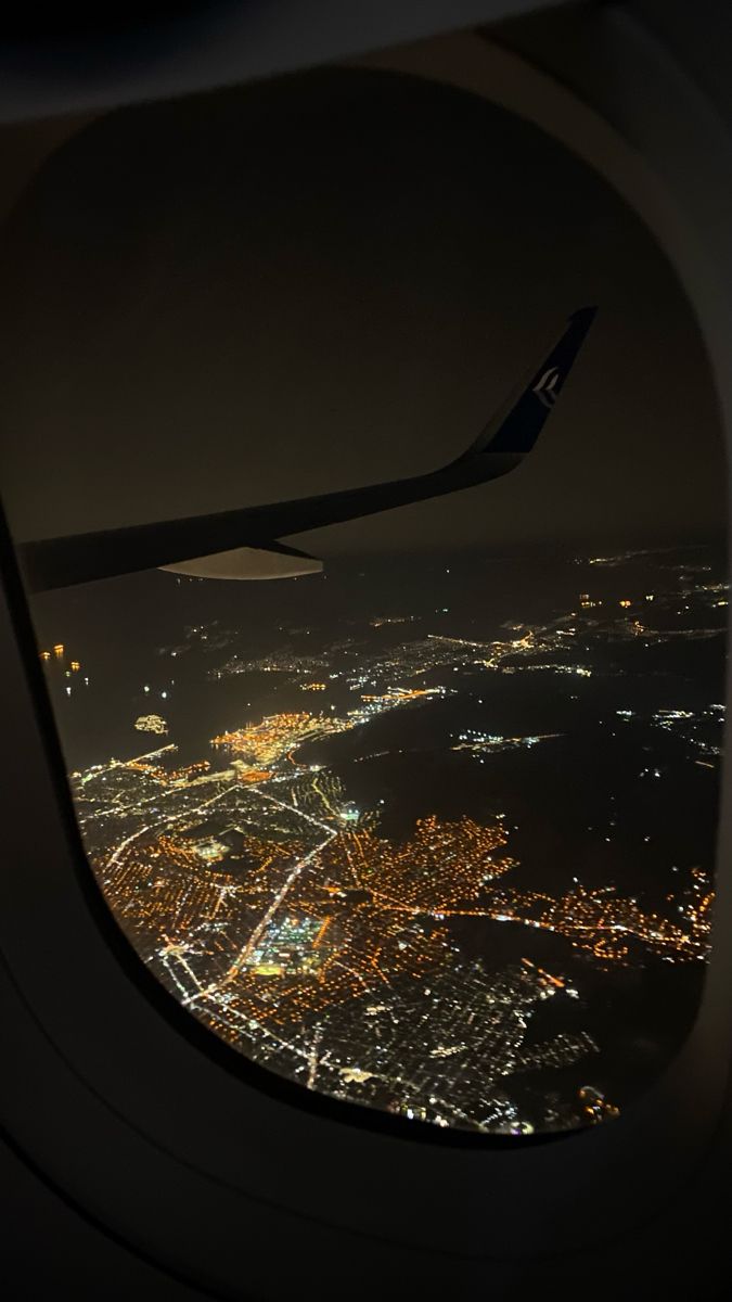 the view from an airplane window at night, looking down on city lights in the distance