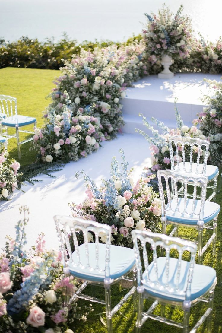 rows of white chairs with blue seats in front of flowers and greenery on the lawn