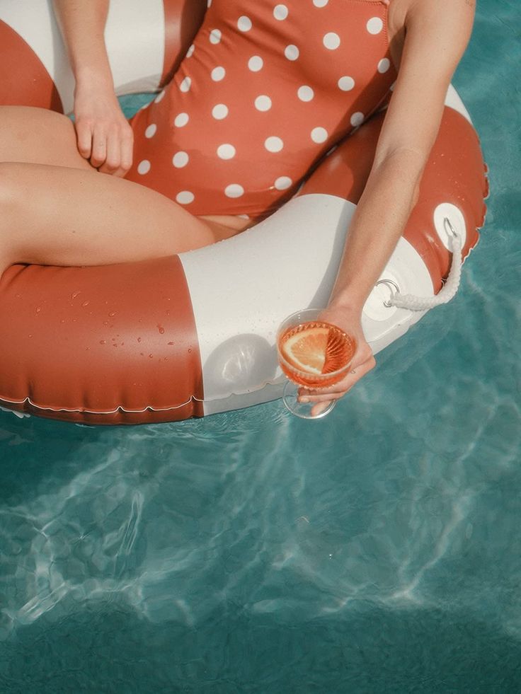 a woman sitting on an inflatable float holding a drink and wearing a polka dot swimsuit