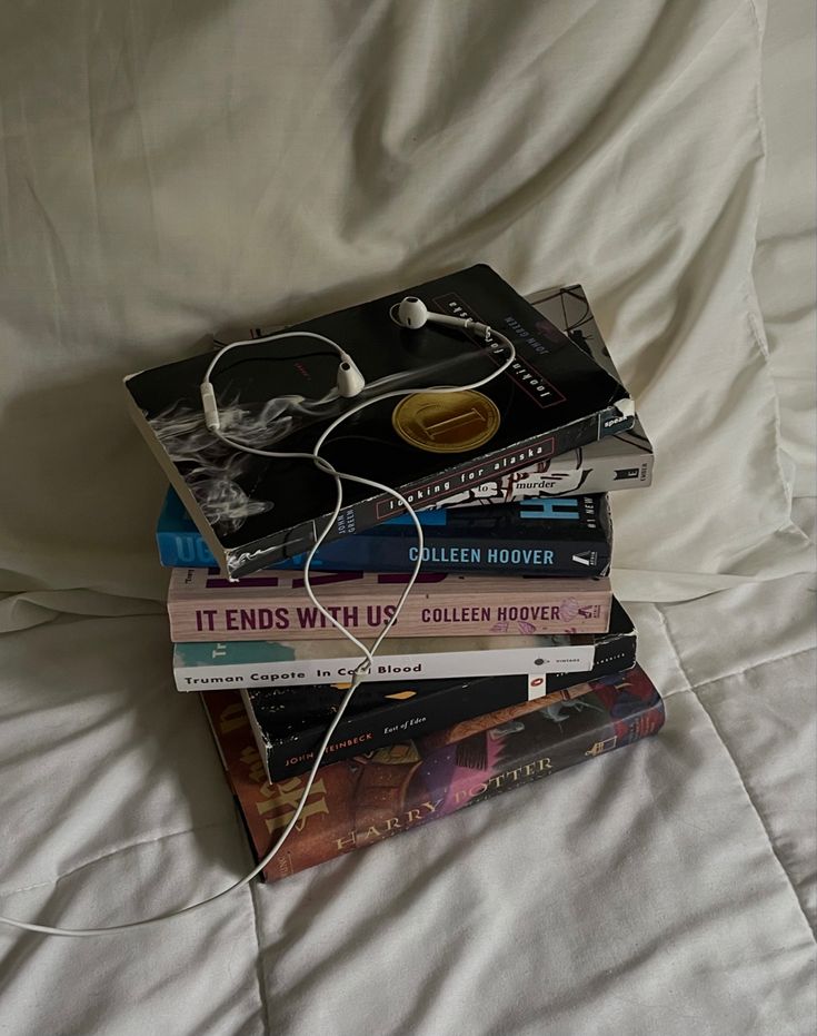 a stack of books sitting on top of a bed next to an ipod charger