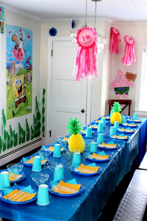 a table set up for a birthday party with blue and yellow plates, pineapples and decorations