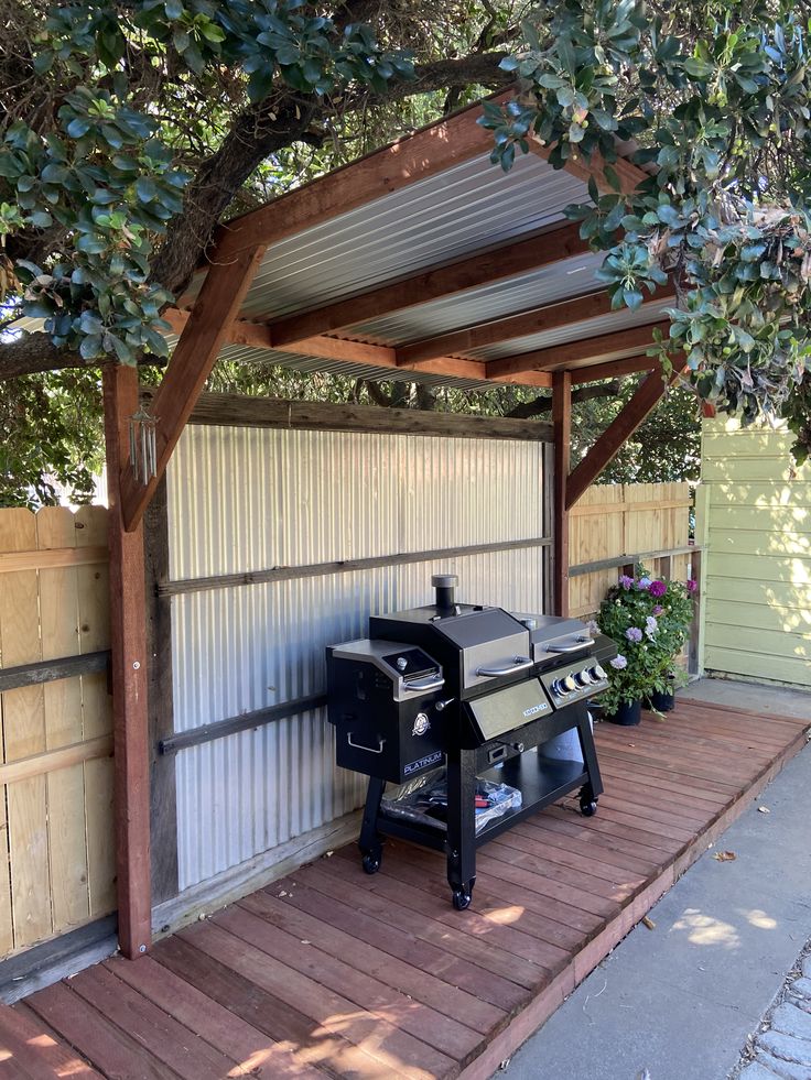 an outdoor bbq grill in the middle of a wooden deck under a large tree