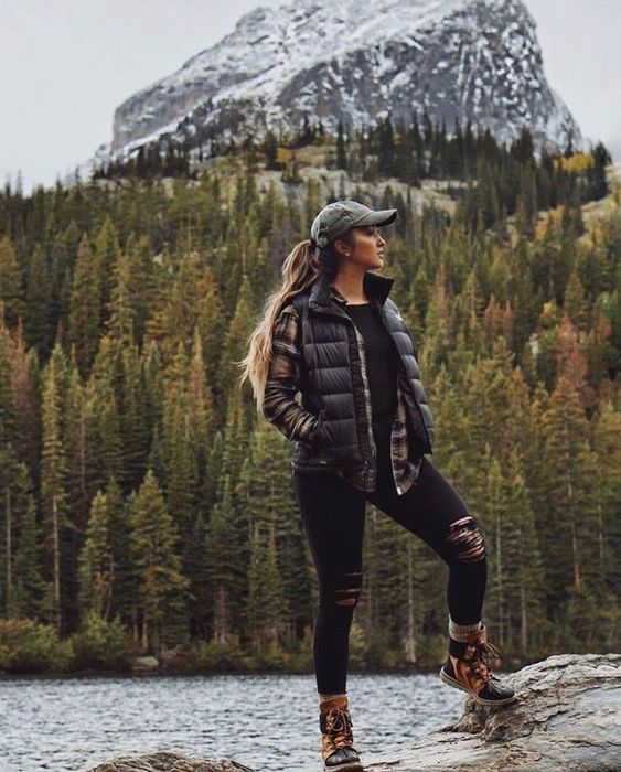 a woman standing on top of a rock next to a lake in the mountains with trees around her