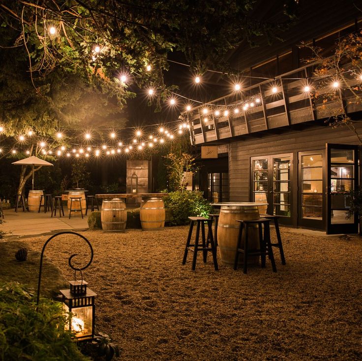 an outdoor patio with lights strung from the ceiling and wooden stools on the ground