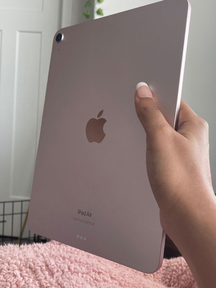 someone holding an ipad in their hand on a pink blanket with a white door behind it