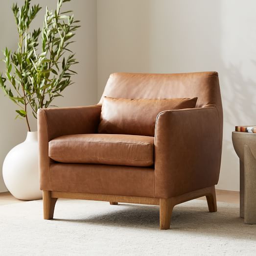 a brown leather chair sitting next to a white vase