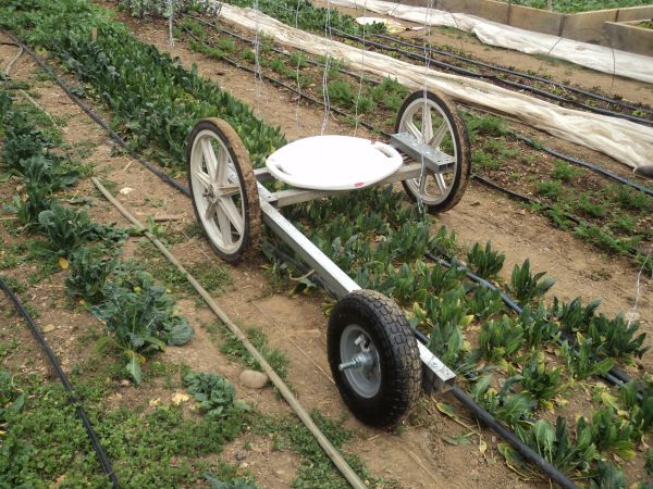 a wheelbarrow is attached to the side of a garden bed with plants growing in it