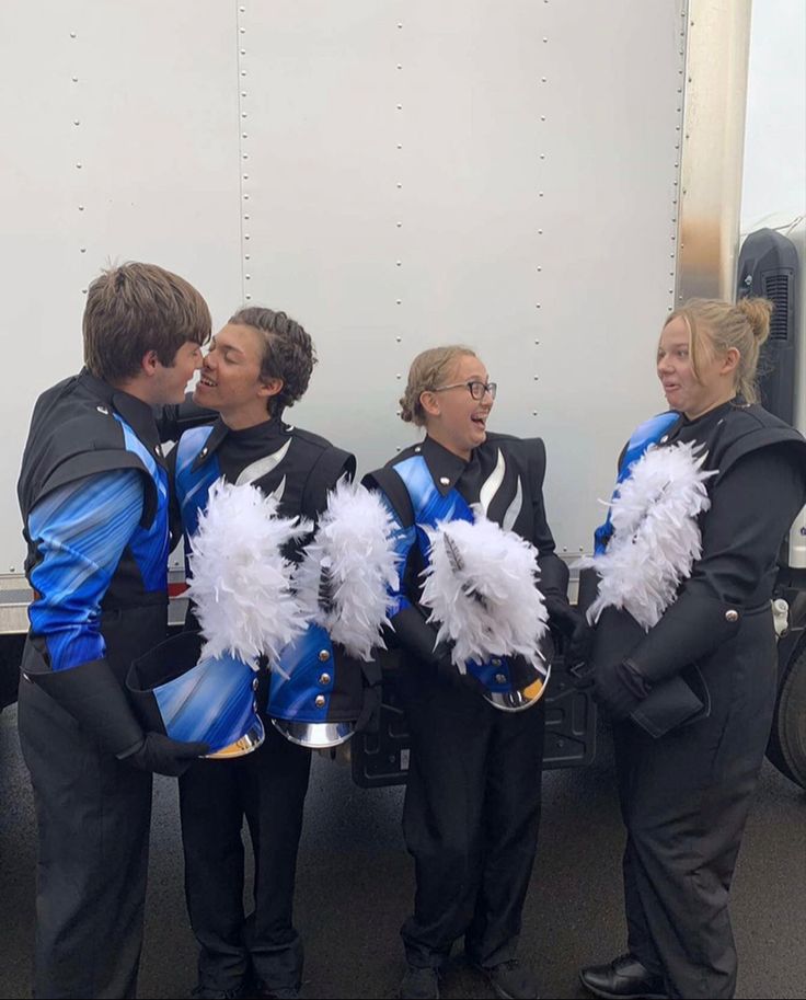 four people dressed in blue and white cheerleaders are standing next to a food truck