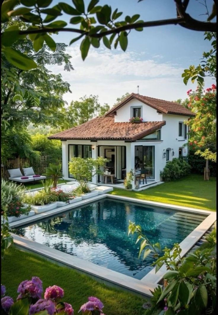 a pool in front of a white house with flowers around it and a patio area