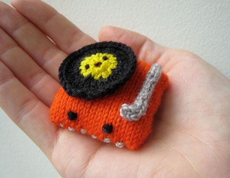 a hand holding a tiny knitted object in the shape of a car with a record on top