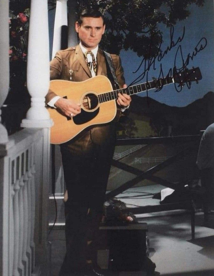 a man in a suit and tie holding an acoustic guitar while standing on a porch