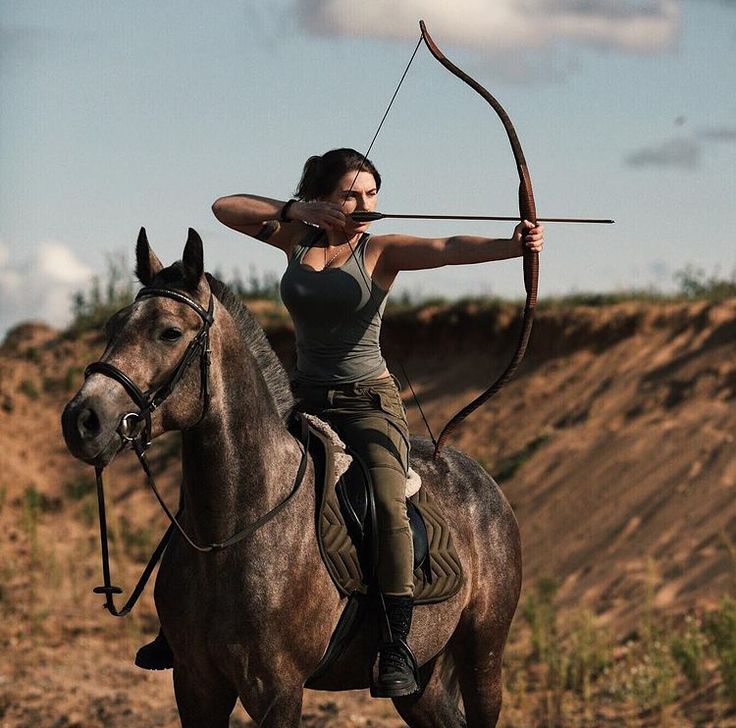 a woman is riding a horse with an arrow in her hand and aiming the bow