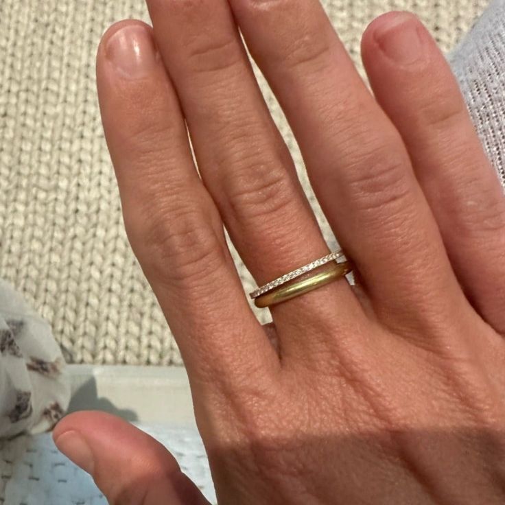 a woman's hand with a gold ring on top of her left hand and a white towel in the background