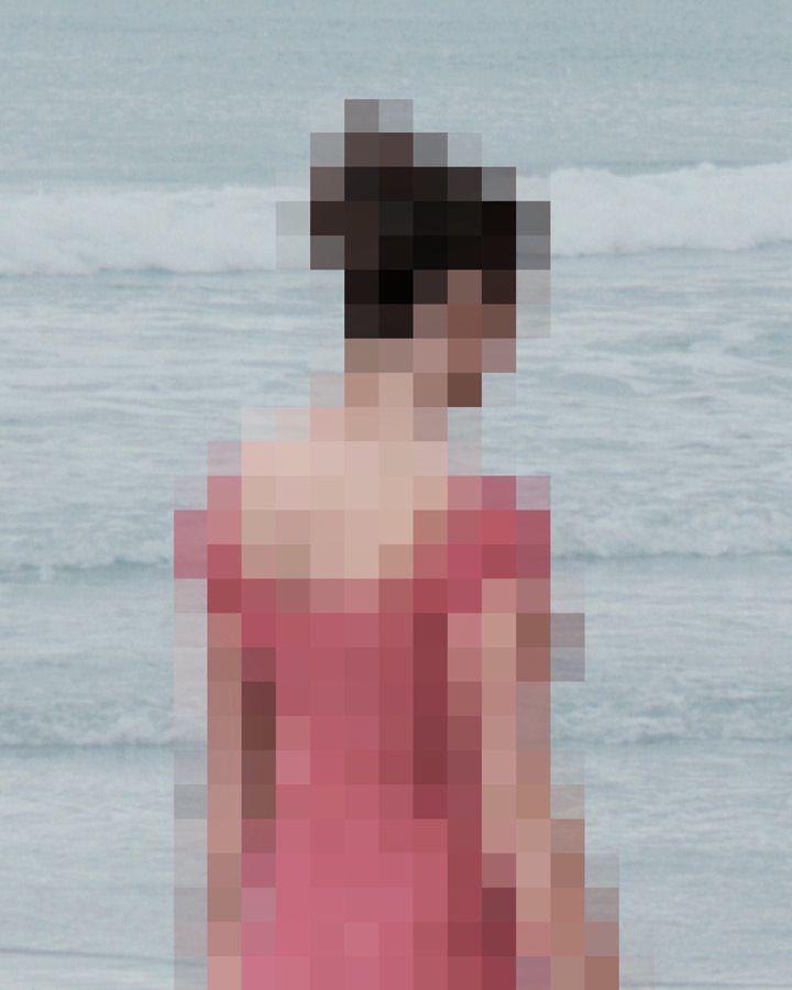 a woman in a pink dress standing on the beach with her back to the camera