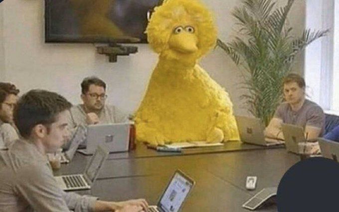 a group of people sitting around a table with laptops and a large stuffed animal