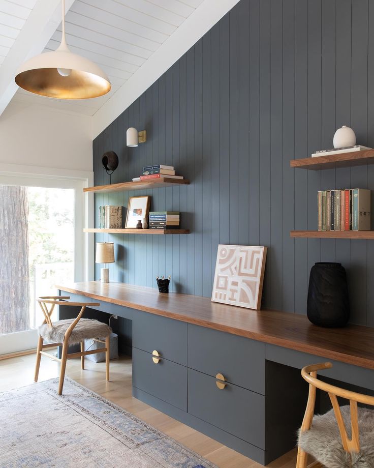 a room with shelves, desk and chairs in the corner next to a large window