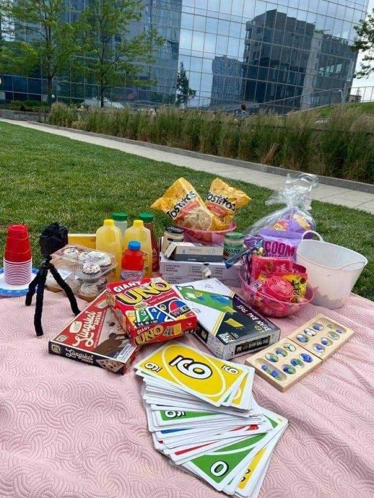 an assortment of snacks on a blanket in the grass near some buildings and water bottles