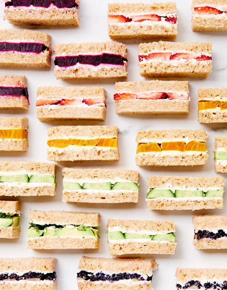 several sandwiches are arranged in rows on a white surface, each with different colored fillings