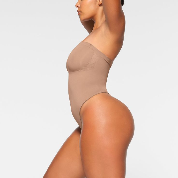 Cinch your waist and sculpt your tummy and core in this perfectly compressive strapless thong bodysuit. Wear it your way with removable adjustable straps that convert to shoulder straps, cross-back, or halter-style. Features center front and side stitching to define and support your bust, and a cotton gusset with snap closure. Fits true to size. | SKIMS Strapless Thong Bodysuit | Medium Neutral | Seamless Sculpt Strapless Shaping Bodysuit With Built-in Bra, Second-skin Bodysuit With Spaghetti Straps And Built-in Bra, High Cut Nylon Bodysuit With Built-in Bra, Solid Strapless Smoothing Bodysuit, Sculpting Backless Swimwear With Built-in Bra, Strapless Smoothing Bodysuit Shapewear, Strapless Stretch Shapewear Bodysuit, Strapless Smoothing Shapewear Bodysuit, Second-skin Shapewear With Built-in Bra And Full Coverage