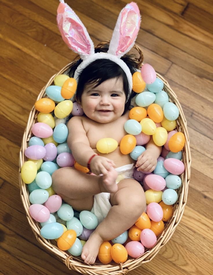 a baby is sitting in a basket filled with candy eggs and an easter bunny ears headband