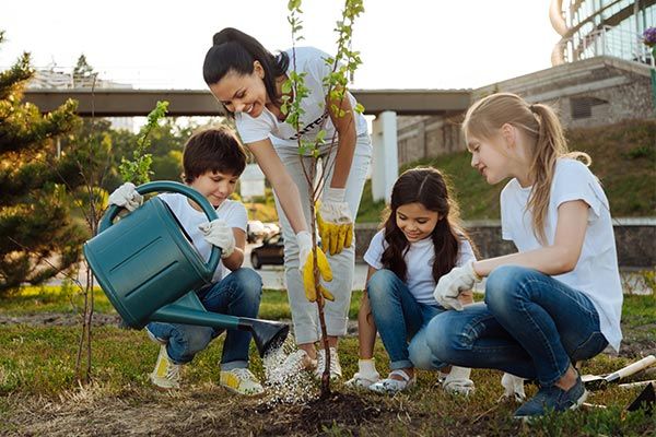 a group of people that are kneeling down in the grass with shovels and plants