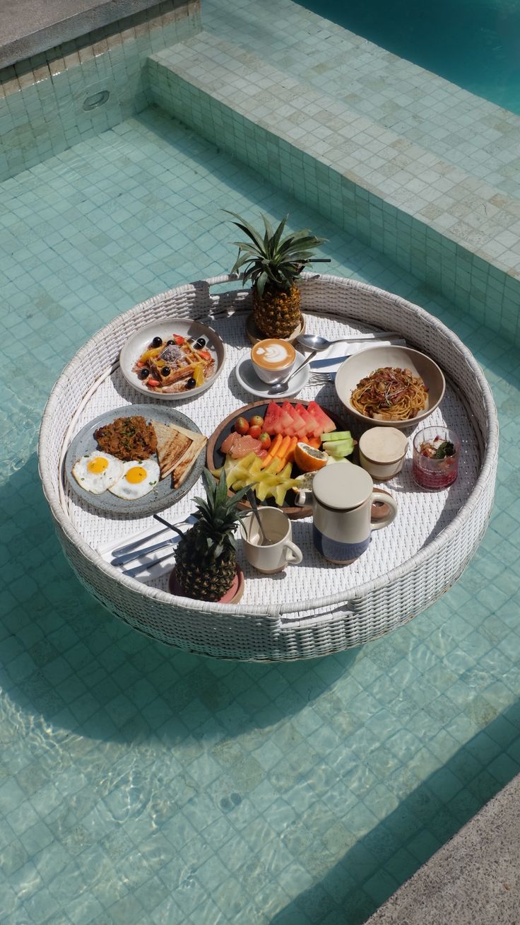 a table that has food on it by the pool in front of a swimming pool