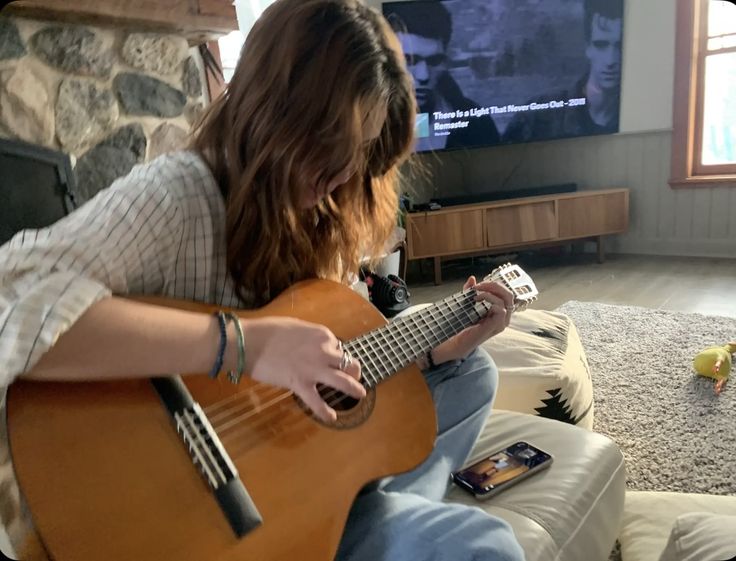 a person sitting on a couch playing a guitar in front of a tv with a remote control