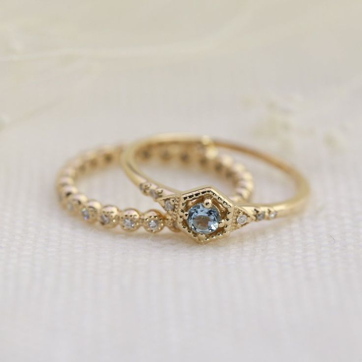 two gold wedding rings with blue and white diamonds on top of each other, sitting on a table