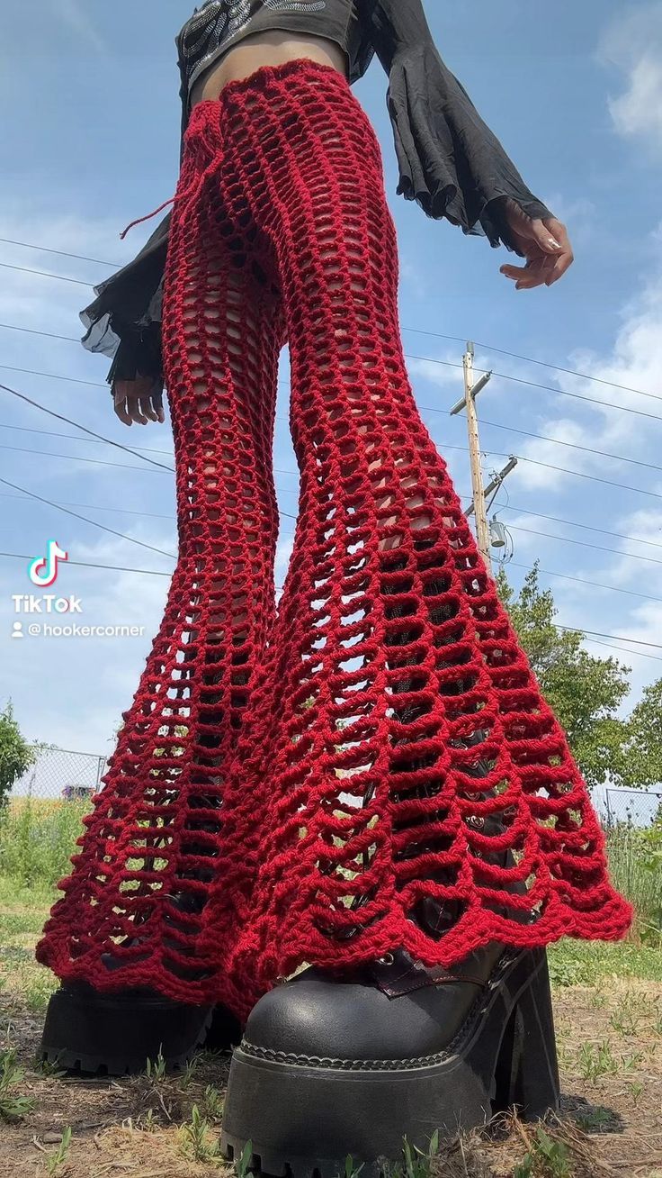 a woman in red crocheted pants standing on top of a black boot with her legs crossed