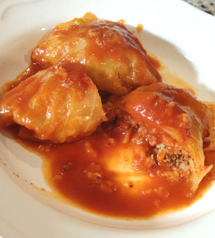 two stuffed cabbages on a white plate covered in gravy and marinara sauce