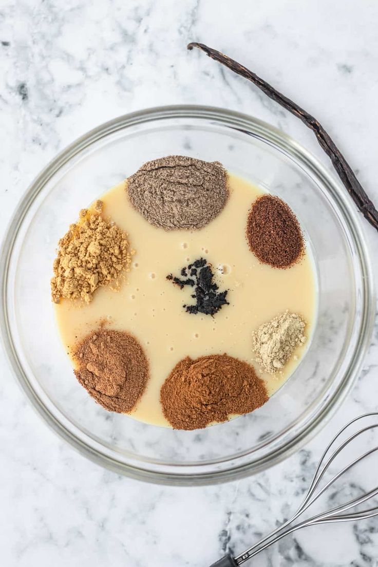 a bowl filled with different types of spices on top of a counter next to a whisk